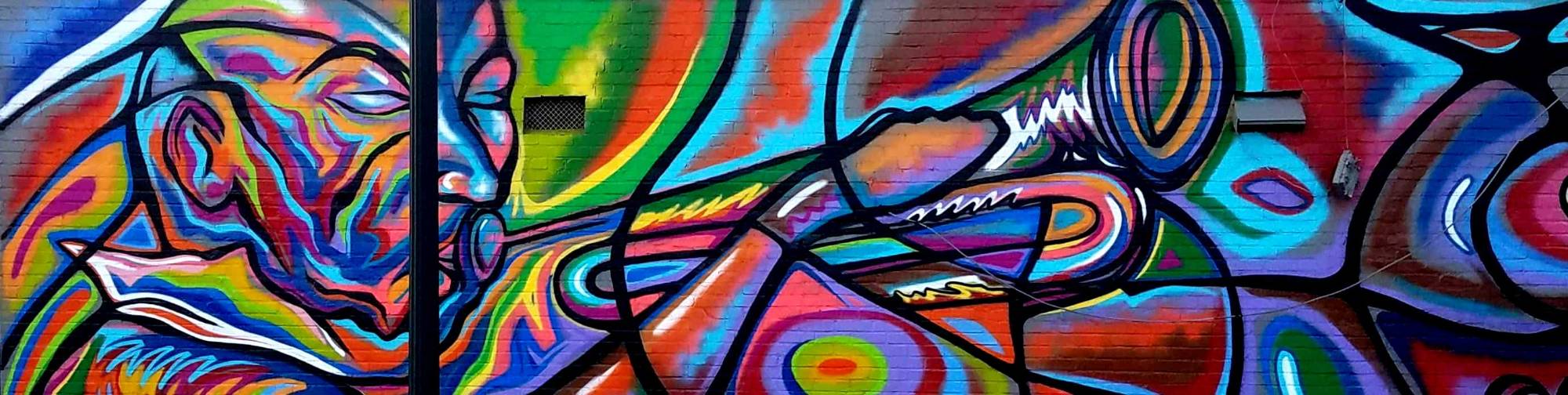Panoramic brick wall mural of a horn player in rainbow colors with bold black outlines