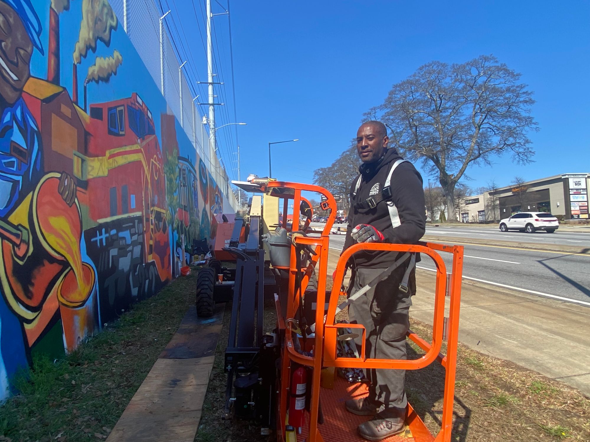 Corey Barksdale on a boom lift beside the finished industrial-heritage panel of the Blandtown mural, Atlanta